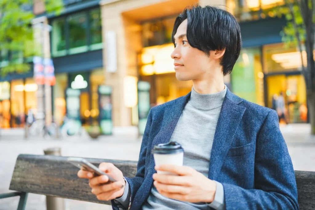 携帯とコーヒーを持つ男性